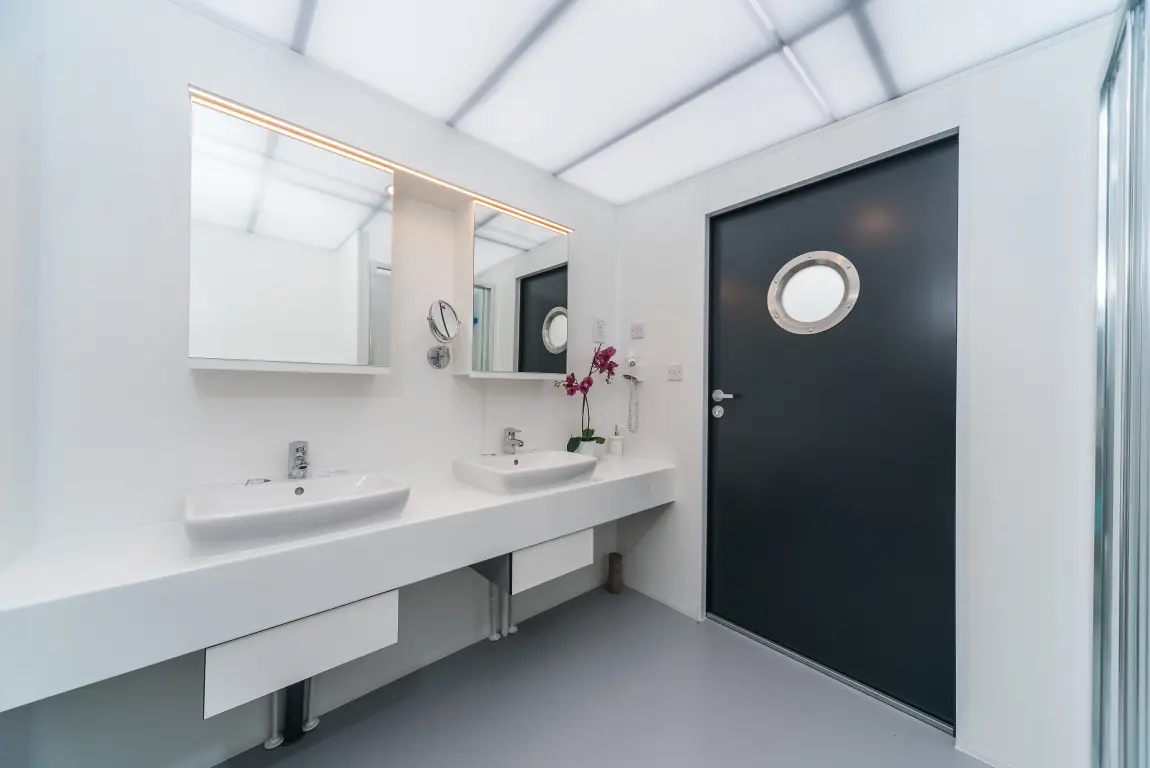 Keramische wastafels met spiegels en LED-verlichting in wit, naast een paarse orchidee en een antracietkleurige deur.