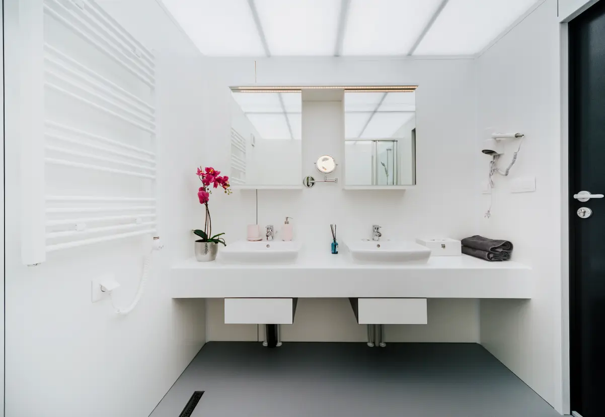 Keramikwaschbecken mit Spiegeln und LED-Beleuchtung in Weiß, daneben eine lila Orchidee und eine anthrazitfarbene Tür.
